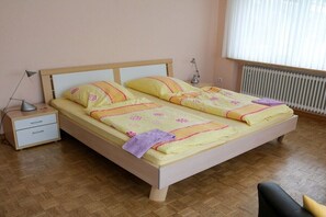 Ein Doppelbett mit Holzrahmen, ein Nachttisch mit Lampe und ein Fenster mit Jalousien.