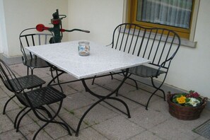 Ein Tisch mit Metallgestell, zwei Stühle, ein kleines Glas und ein Korb mit Blumen.