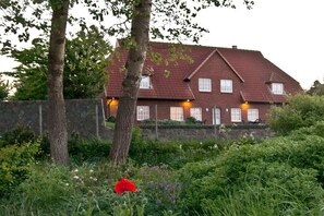 A brick house with a sloped roof, surrounded by a stone wall and lush greenery. - Nolte - Guesthouse Holnis (Glücksburg)