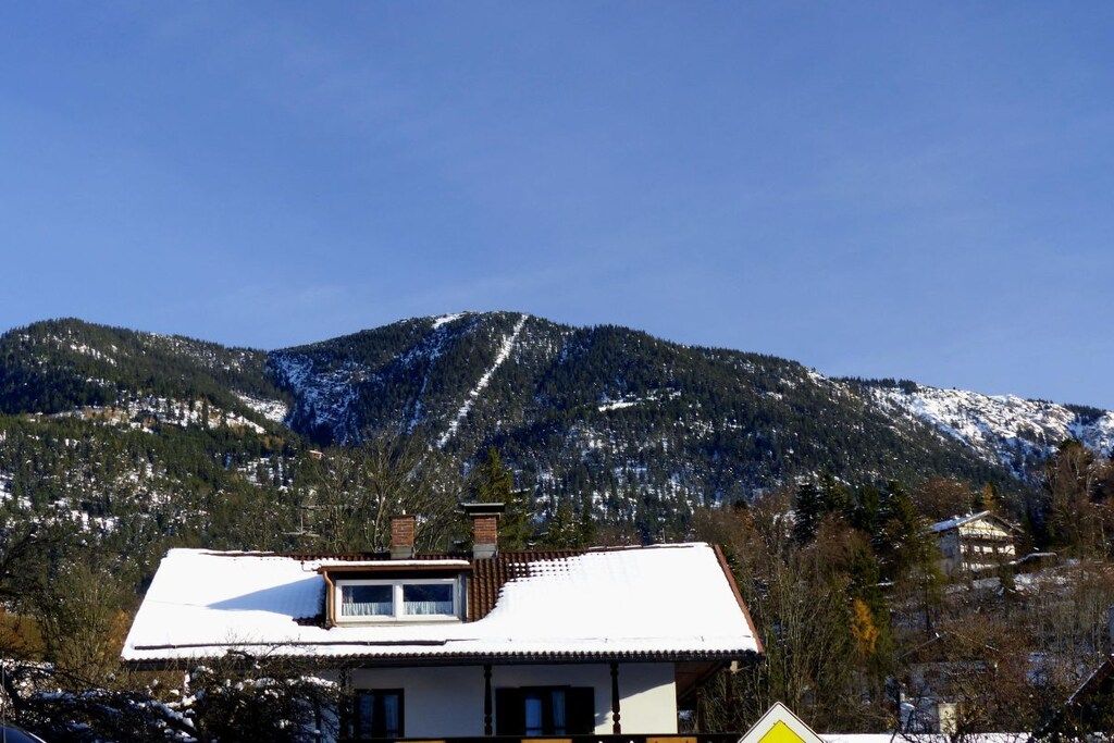 Une maison dont le toit est recouvert de neige, avec une cheminée bien visible, et une montagne en arrière-plan.
