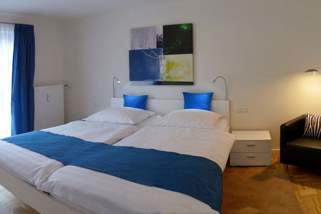 Un lit double avec une literie blanche et bleue, une table de chevet avec une lampe et un canapé noir.