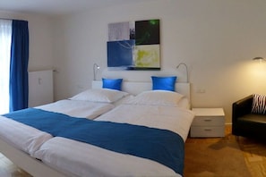 A double bed with white and blue bedding, a nightstand with a lamp, and a black couch. - Holiday apartment with 3 bedrooms (Garmisch-Partenkirchen)