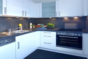 A modern kitchen with white cabinets, a black countertop, a stove, and an oven. - Holiday apartment with 3 bedrooms (Garmisch-Partenkirchen)