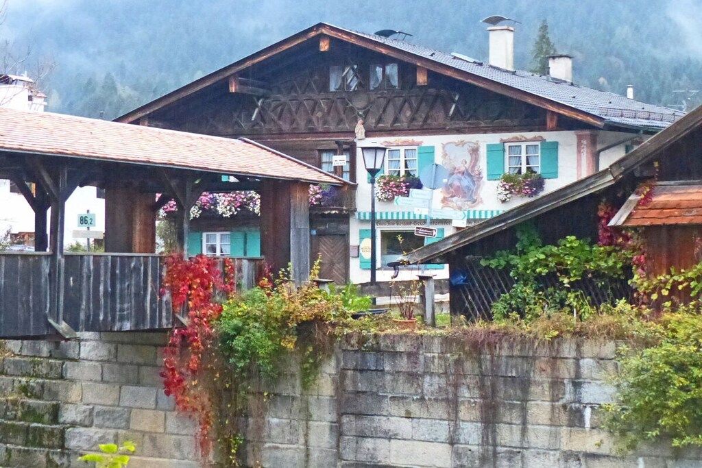 Um chalé tradicional com fachada de madeira, uma parede de pedra em primeiro plano e montanhas ao fundo.