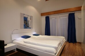 A bedroom with a double bed, a bedside table, a nightstand, a wall-mounted artwork, and a window with curtains. - At the spa park - Apartment 3 - 150 sqm (Garmisch-Partenkirchen)