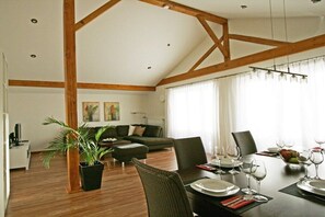 Ein Essbereich mit Holzboden, einer Couch, einem Esszimmertisch mit Tellern und Gläsern sowie einer Zimmerpflanze.