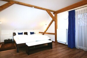 Un dormitorio con techo de madera, cama con ropa de cama blanca, mesita de noche y ventana con cortinas azules.