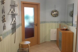Een badkamer met een houten deur, een klein krukje, een kast en decoratieve wandversieringen.
