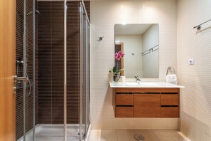 Een moderne badkamer met een douche met glazen wand, een houten wastafelmeubel en een grote spiegel.