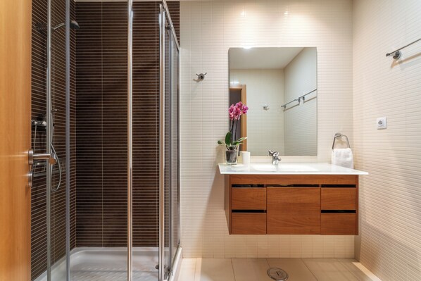 Un baño moderno con ducha de vidrio, tocador de madera y un espejo grande.