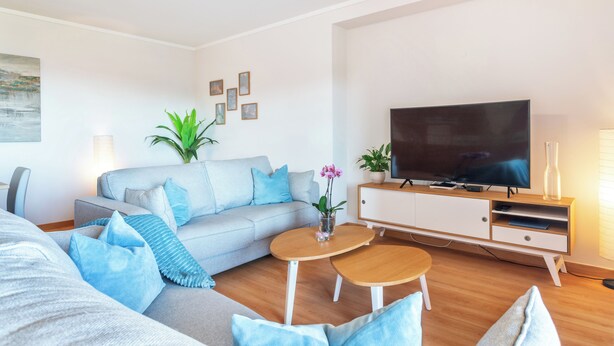 Un soggiorno moderno con un divano grigio, due tavolini, una TV a schermo piatto e un mobile.