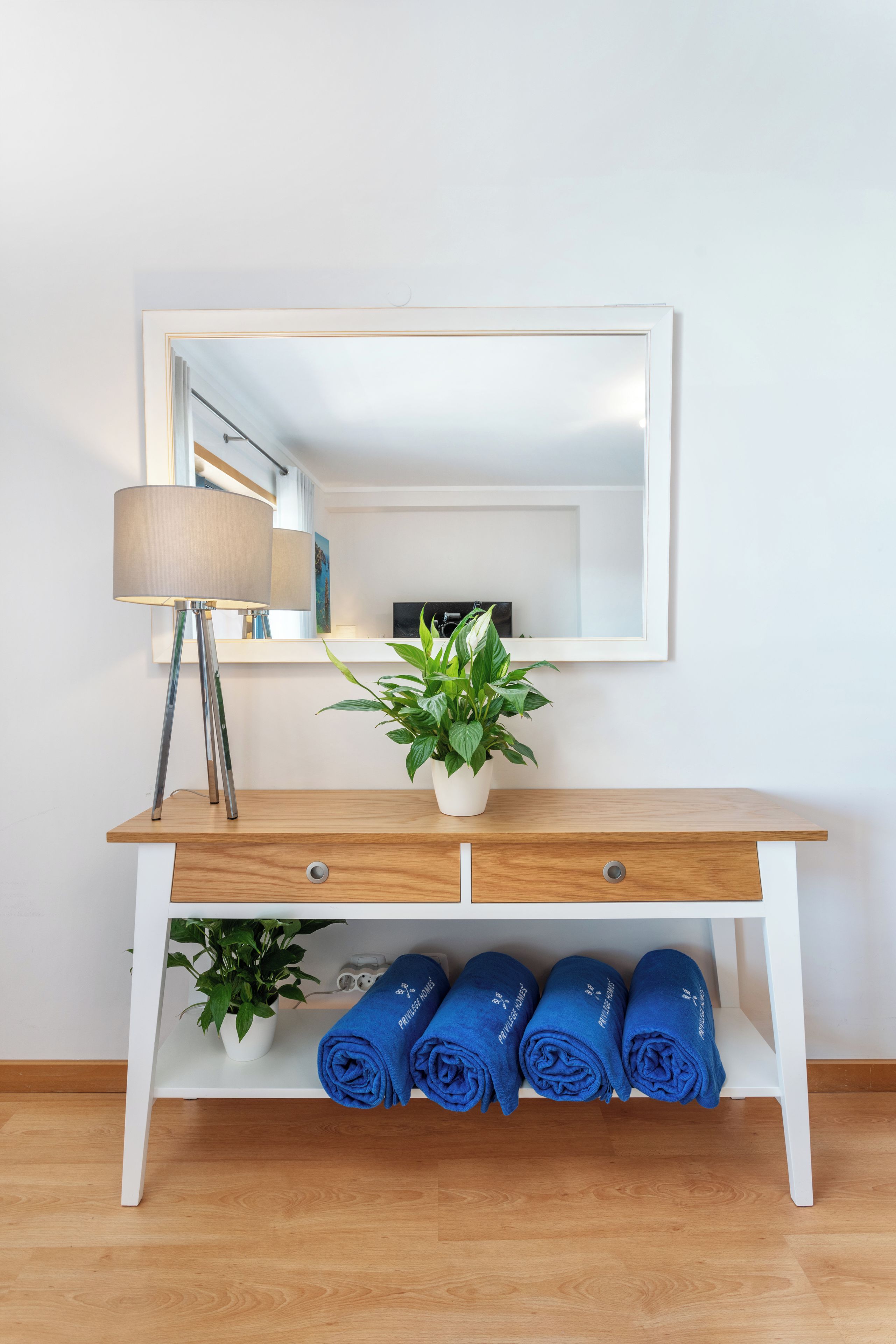 A white console table with a mirror above it, a lamp to the left, and a potted plant in the center.