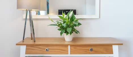 A white console table with a mirror above it, a lamp to the left, and a potted plant in the center.