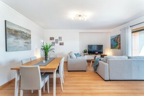 Una sala moderna con una mesa de comedor de madera, un sofá gris y un televisor de pantalla plana.