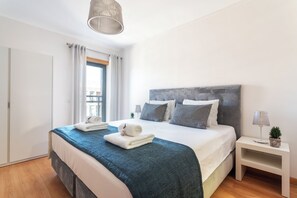 Un dormitorio moderno con una cama grande, una mesita de noche, una lámpara y vistas al exterior.