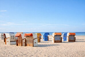 Bungalôs de praia com números, dispostos numa praia arenosa com o mar ao fundo.