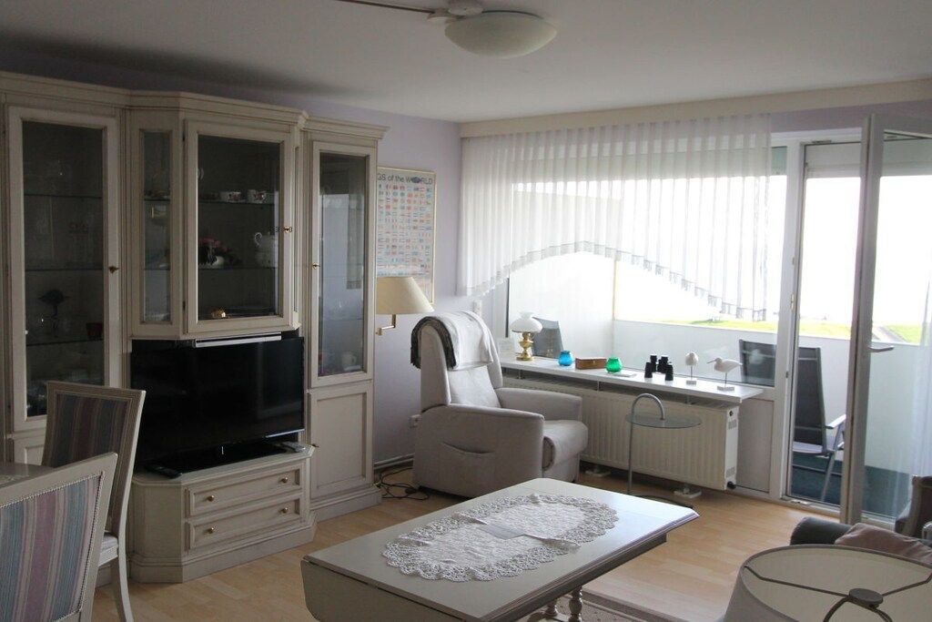 A living room with a television, a dining table, a sofa, and a window with blinds.