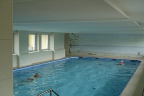 An indoor swimming pool with clear water, a diving board, and a view of the beach through the windows. - Apartment CuxNautic414 (Cuxhaven)