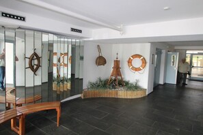 A lobby with a curved wooden bench, a wall-mounted life preserver, and a wooden easel. - Apartment CuxNautic414 (Cuxhaven)