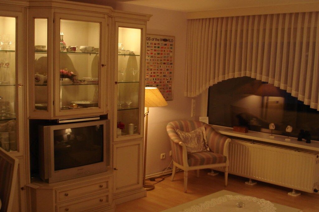 A living room with a cabinet, a television, a lamp, a chair, and a poster on the wall.