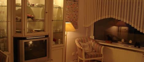 A living room with a cabinet, a television, a lamp, a chair, and a poster on the wall.