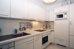 Una cocina con armarios blancos, microondas, estufa y pileta.