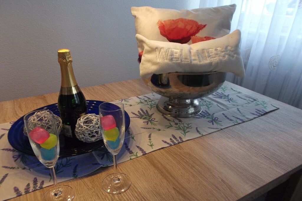 A table with a bottle of champagne, two glasses with colorful ice cubes, and a decorative bowl with a cushion.