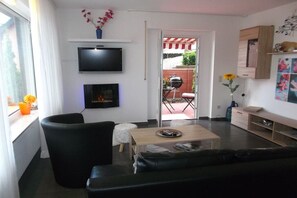 A modern living room with a flat-screen TV, a fireplace, a sofa, a coffee table, and a view through an open door to an outdoor patio area. - "To the Moselle View" (Reil)
