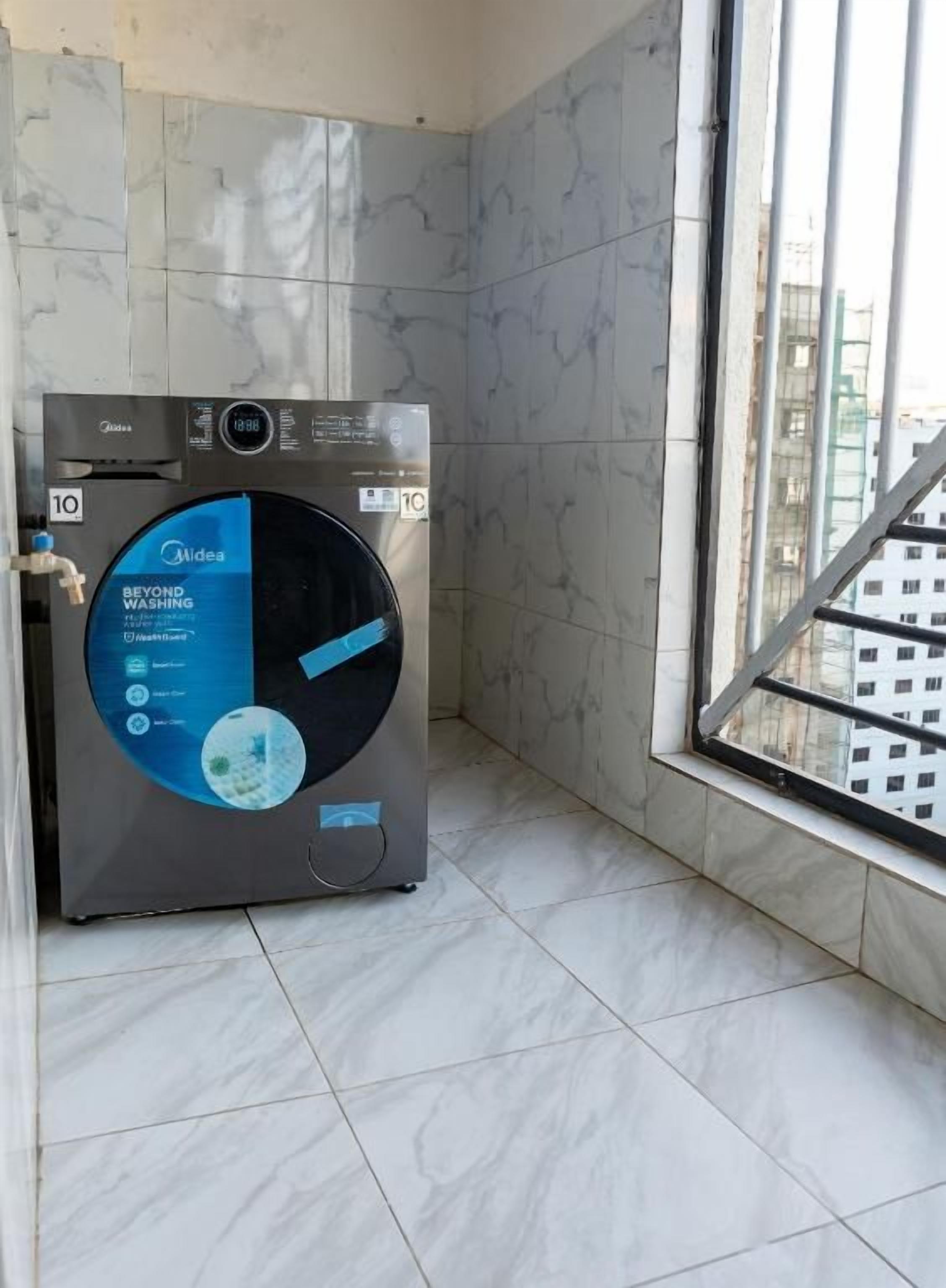Una lavadora compacta y moderna en un rincón de una habitación con un ventanal grande.