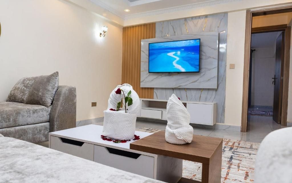 A modern living room with a flat-screen TV, a sofa, a coffee table, and a decorative plant.