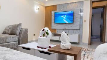 A modern living room with a flat-screen TV, a sofa, a coffee table, and a decorative plant.