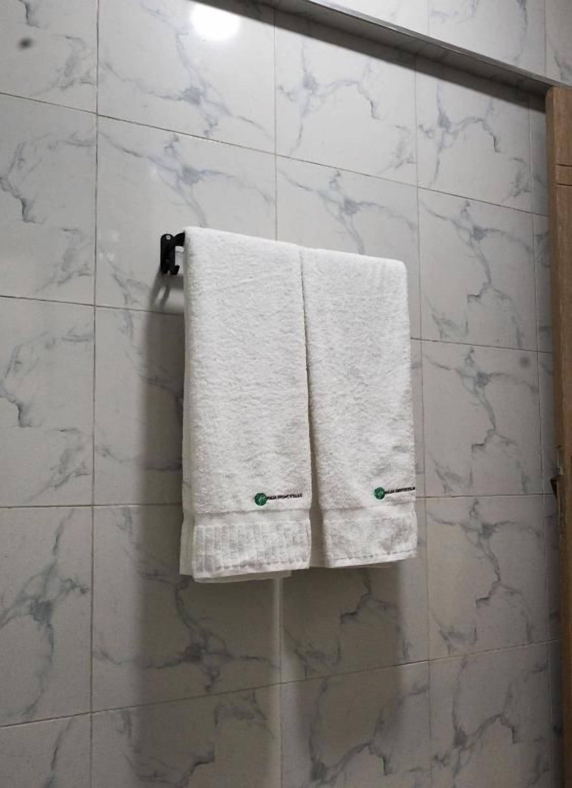 Un baño con azulejos de mármol blanco y dos toallas colgadas en un perchero.