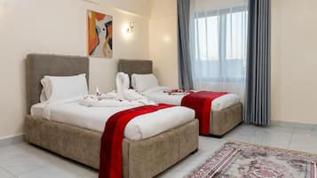 A hotel room with two beds, a large window with curtains, a patterned rug, and a wall-mounted light fixture.