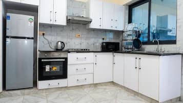 Una cocina con armarios blancos, un refrigerador de acero inoxidable, un microondas y una estufa.