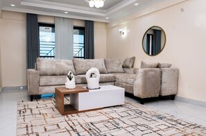 A living room with a sectional sofa, a coffee table, and a large mirror on the wall. - Palm Grove Villas (Nairobi)