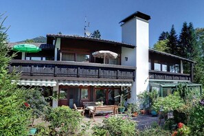 A two-story building with a balcony, outdoor seating, and a garden area. - 1 in the Sonnenbichl house (Walchensee)