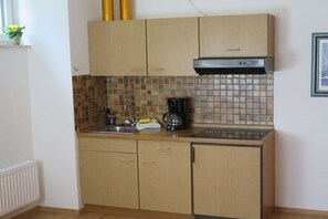 A compact kitchen with wooden cabinets, a tiled backsplash, a coffee maker, and a built-in stove. - 1 in the Sonnenbichl house (Walchensee)