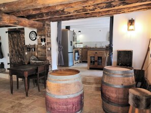 A rustic interior with wooden barrels, a dining table, and a kitchen area.