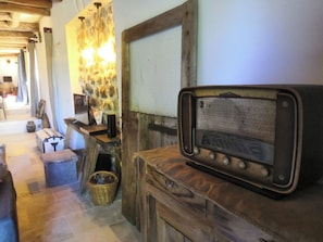 A rustic interior with a vintage radio on a wooden cabinet, a stone wall with a textured pattern, and a wooden door.