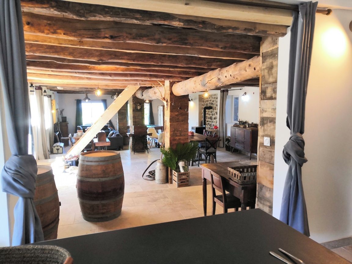 Een interieur met zichtbare houten balken, een eethoek met een tafel en stoelen, en een grote vaten.