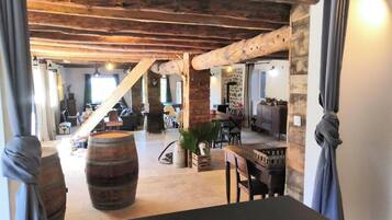 Een interieur met zichtbare houten balken, een eethoek met een tafel en stoelen, en een grote vaten.