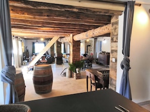 An interior with exposed wooden beams, a dining area with a table and chairs, and a large barrel.