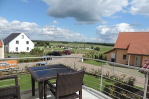 Ein Balkon mit Korbmöbeln, der auf einen Wohnbereich mit Häusern und einer Straße blickt.