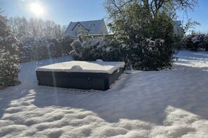 Ein verschneiter Außenbereich mit einem großen, schwarzen Objekt, vermutlich einem Möbelstück, und einem Haus im Hintergrund.
