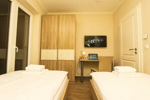 Ein Hotelzimmer mit zwei Betten, einem Schreibtisch mit einem Laptop, einem Fernseher und einem Kleiderschrank.