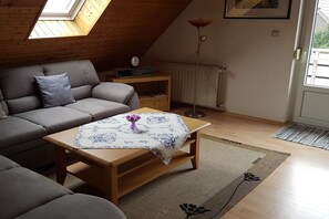 A cozy living room with a sofa, a wooden coffee table with a floral tablecloth, a floor lamp, and a radiator. - Holiday apartment with 2 bedrooms (Norden)