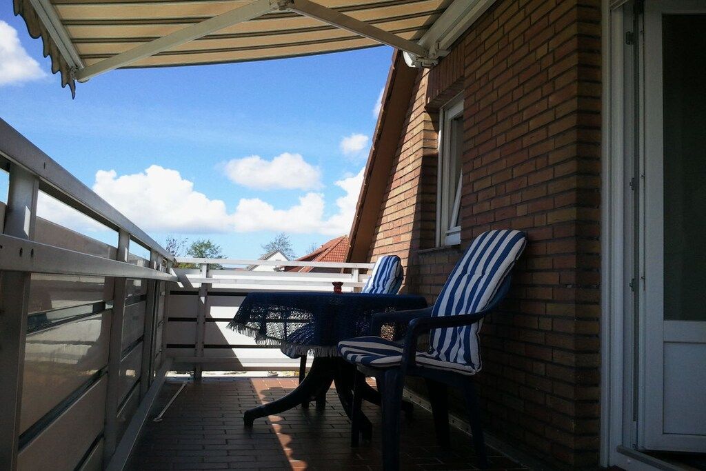 Un espace extérieur abrité, aménagé avec deux chaises à rayures et une table, situé à côté d’un bâtiment en briques.