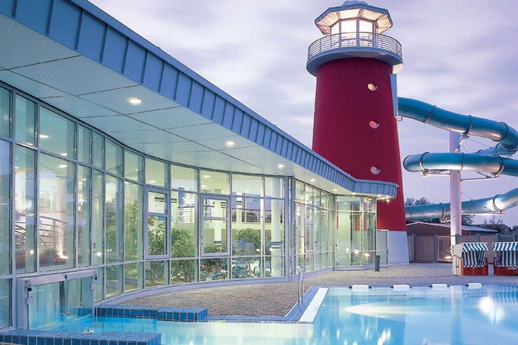 Une piscine dotée d’une structure en forme de phare rouge et de murs en verre.