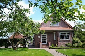 A two-story brick house with a front entrance, a visible window, and a tree in the foreground. - Holiday apartment with 1 bedroom (Osteel)