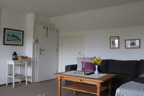 Een woonkamer met een houten tafel, een bank, een witte deur en een kleine witte tafel met een mand en een lantaarn.